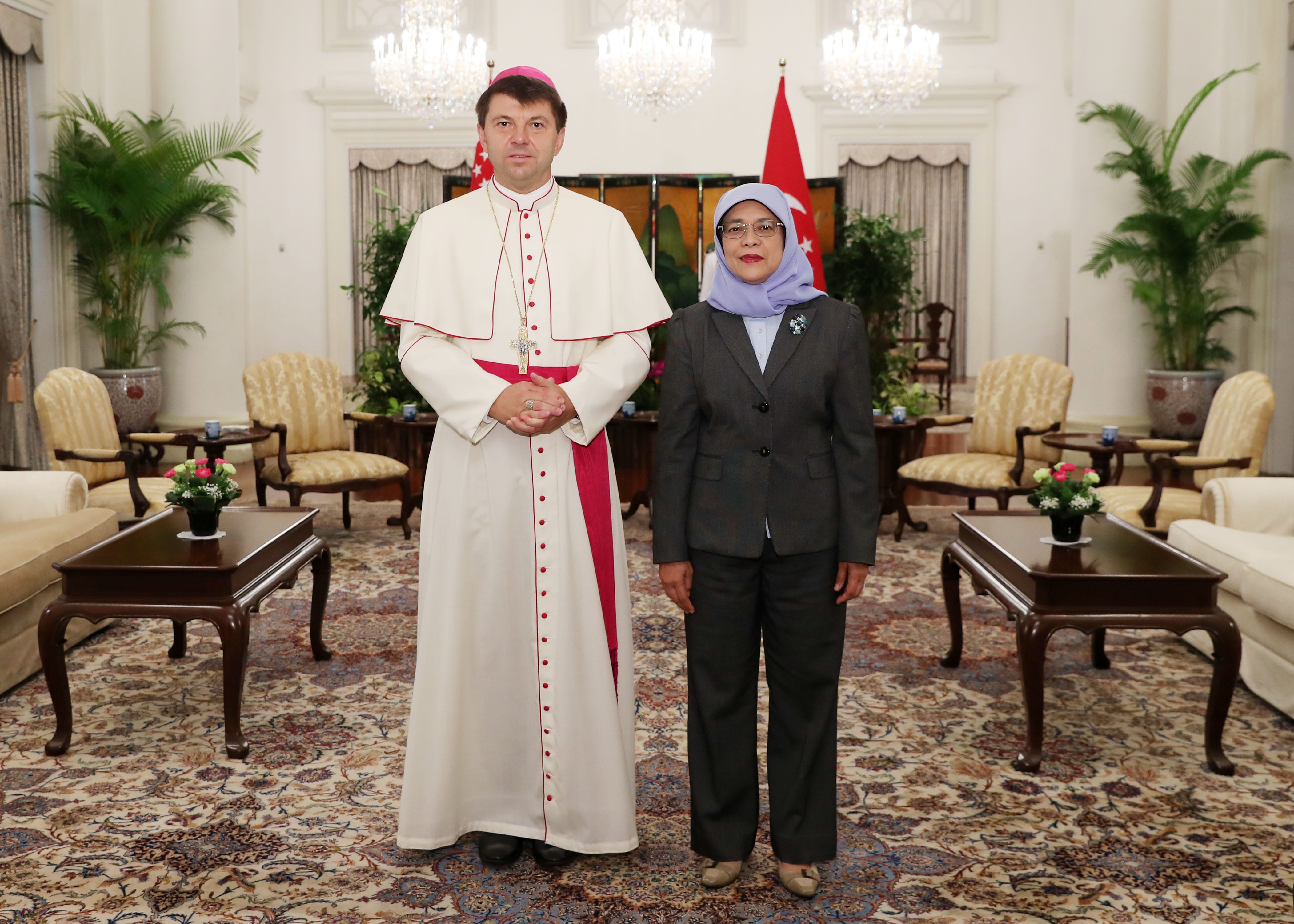 Man in religious garb and woman in business suit stand side-by-side indoors.